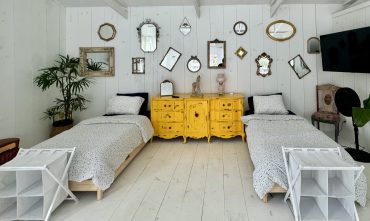 Twin beds with white linens, vintage yellow dresser between them, wall of mirrors above