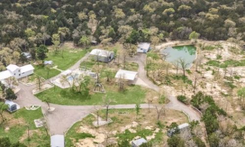 An aerial view of a rural property with several small buildings, a pond, and surrounding trees.